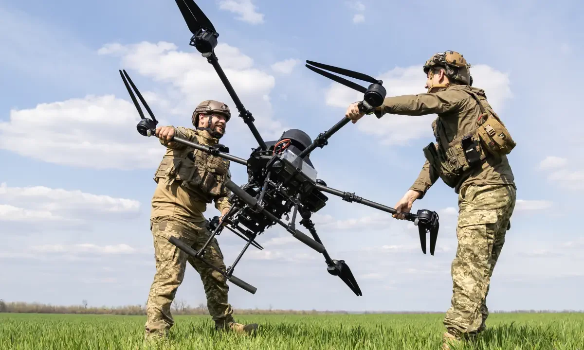 Δύο στρατιώτες ρυθμίζουν βαρύ drone «Baba Yaga» σε χωράφι.