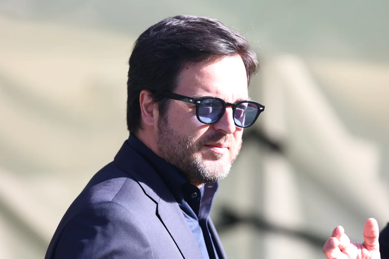 Ο άνδρας εμφανίζεται με σκούρο κοστούμι και γυαλιά ηλίου, σε κοντινό στιγμιότυπο με φόντο κερκίδες. Η εικόνα αποπνέει σοβαρότητα και ταιριάζει σε θέμα που αφορά διοικητικές ή μεταγραφικές εξελίξεις στην ΑΕΚ. Πηγή: ΙΝΤΙΜΕ.