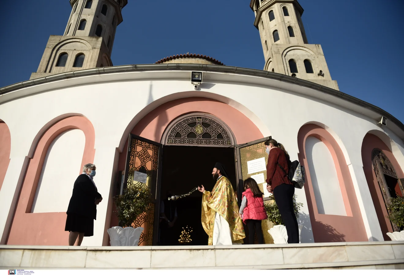 Περιγραφή εικόνας: Ιερέας στην είσοδο ορθόδοξου ναού υποδέχεται πιστούς, με το εορτολόγιο και τις θρησκευτικές ημέρες να βρίσκονται στο επίκεντρο.  Πηγή: ΙΝΤΙΜΕ