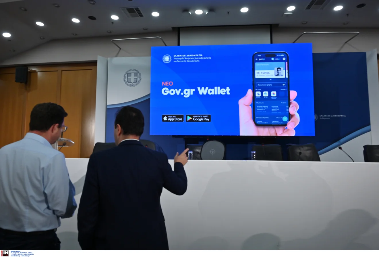 Δύο άνδρες βρίσκονται στην αίθουσα παρουσίασης του νέου Gov.gr Wallet, με την εφαρμογή να προβάλλεται σε μεγάλη οθόνη. Πηγή: INTIME.