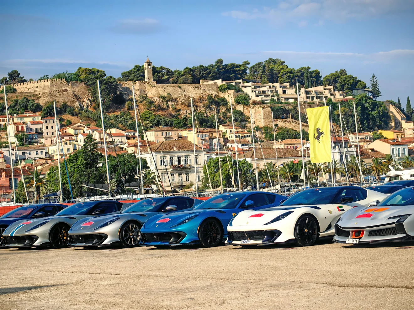 Σειρά από Ferrari είναι παραταγμένες σε λιμάνι, με φόντο ιστιοπλοϊκά, παραθαλάσσια πόλη και κάστρο. Η εικόνα ταιριάζει σε θέμα για τη Ferrari, την πολυτέλεια και την αυτοκίνηση. Πηγή: ΙΝΤΙΜΕ.