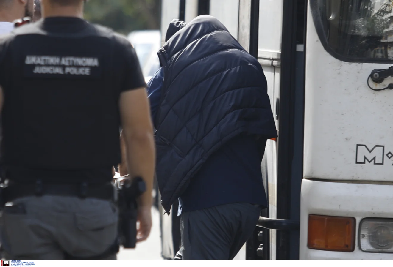 Άτομο με καλυμμένα χαρακτηριστικά οδηγείται σε όχημα της αστυνομίας, παρουσία άνδρα της Δικαστικής Αστυνομίας. Πηγή: ΙΝΤΙΜΕ.