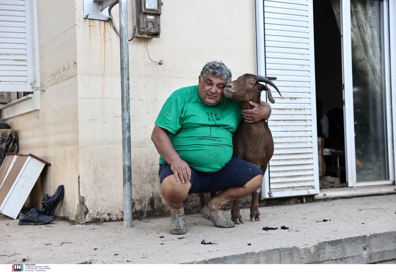 Άνδρας κάθεται έξω από κατοικία αγκαλιά με κατσίκα, σε στιγμιότυπο καθημερινότητας που αποτυπώνει ανθρώπινη επαφή και ζωή στην ύπαιθρο. Πηγή: ΙΝΤΙΜΕ.